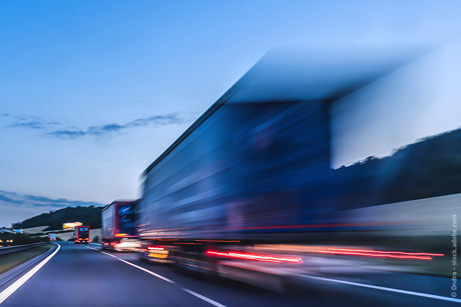 The image shows several trucks on the left lane of a highway. They are shown blurred, highlighting their high speed.