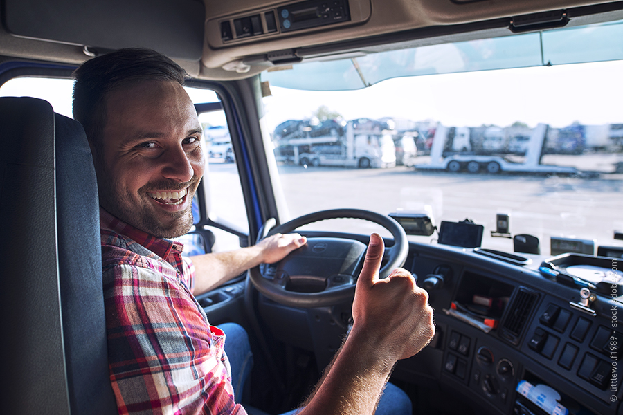 A man sits behind the wheel of a truck, smiling and giving thumbs up.