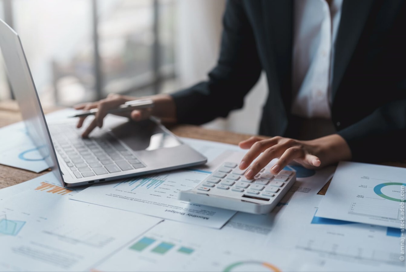 Optimising freight costs_Person sitting at a laptop calculating with a calculator